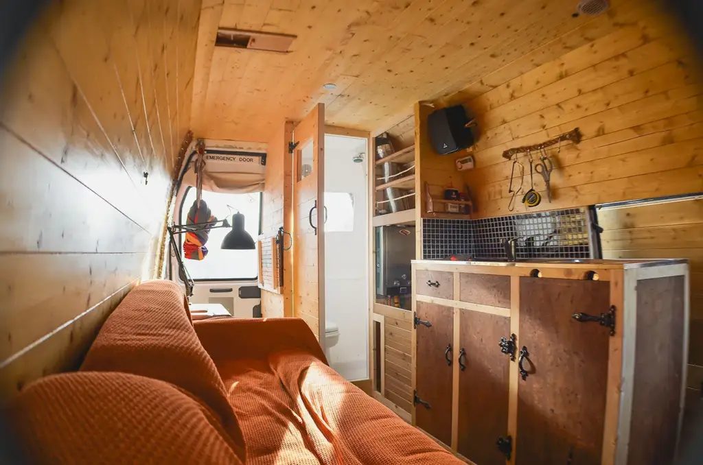 The finished van interior — timber cladding, a small kitchen unit and a made-up bed.